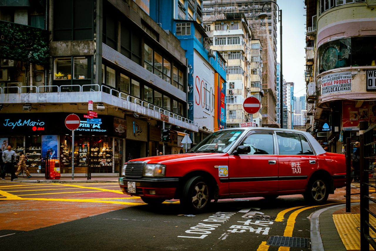 A red taxi on a street lined with tall buildings, Hong Kong